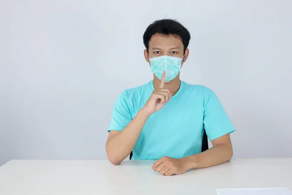 外科用マスクを身に着けている若いアジア人男性は 白い背景に隔離された の印として彼の鼻に手をもたらします — ストック写真