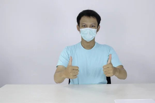 若いアジアの男は自信を持ってジェスチャーでOkの手のサインを与える医療マスクを着用 青いシャツを着たインドネシア人男性 — ストック写真