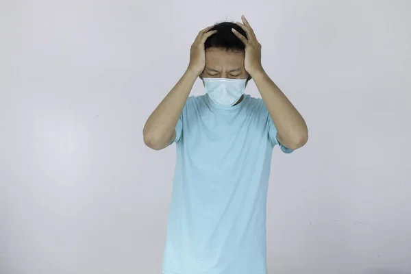 医者のマスクをした若いアジアの男は 重度の頭痛に苦しんでいます 寺院に指を押す 無力顔の表情で痛みを和らげるために目を閉じます — ストック写真