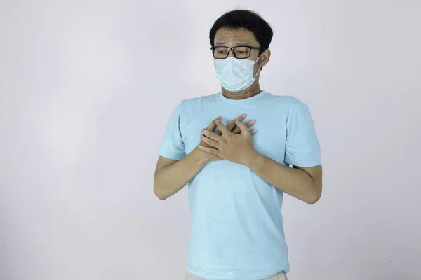 Young asian man with Heart attack or cold flu feeling breathless. He wears a surgical mask and also feels tightness of chest during quarantine life at home. Corona virus outbreak.