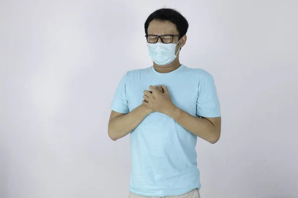 心臓発作や風邪のインフルエンザと若いアジア人男性は息を感じている 外科用のマスクを着用し 自宅での隔離生活でも胸の圧迫感を感じる コロナウイルス発生 — ストック写真