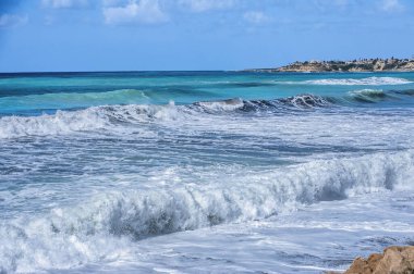 Taze bir bahar rüzgarı dalgaları Kıbrıs kıyılarına sürüklüyor. Akdeniz koyu morötesi deniz ile boyanmıştır ve içeriden parlak bir gök mavisi..     