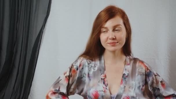 Видео рыжая женщина в сером пеньюаре в интерьере дома — стоковое видео
