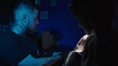 Shooting of man doing dark tattoo of snake for woman