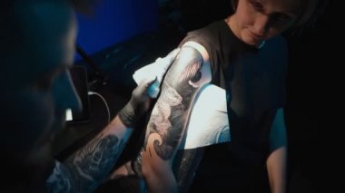 Shooting of man doing dark tattoo of snake on woman in studio