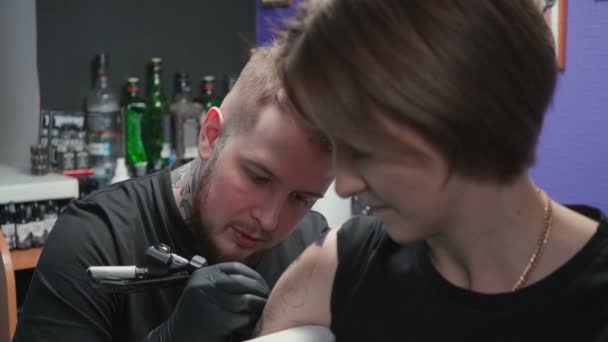 Видео, где мужчина делает тёмную татуировку для женщины в студии — стоковое видео