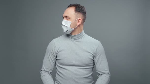 Молодой человек в серой водолазке в медицинской маске — стоковое видео