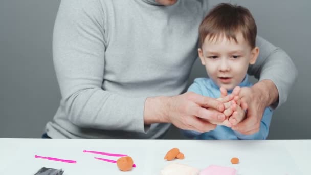 Vidéo de père et fils sculptant des jouets de plasticine sur fond gris — Video