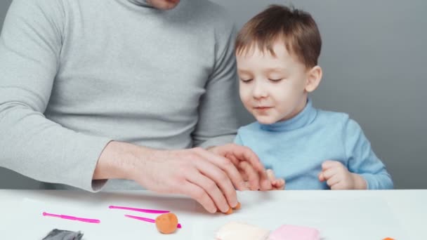 Disparos de padre e hijo esculpiendo juguetes de plastilina sobre fondo gris — Vídeos de Stock