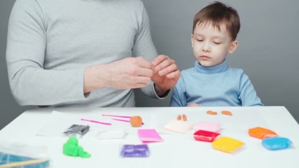 Schieten van vader en zoon beeldhouwen speelgoed uit plasticine op grijze achtergrond — Stockvideo
