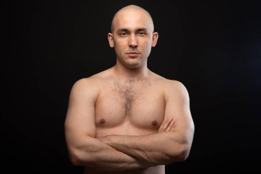 Çıplak omuzlu ve kollarını kavuşturmuş kel bir adamın görüntüsü.
