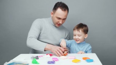 Baba ve oğlunun gri arka planda plastikinden hayvan heykeli yaptığı video.
