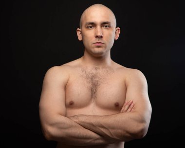 Çıplak omuzlu ve kollarını kavuşturmuş kel bir adamın fotoğrafı.