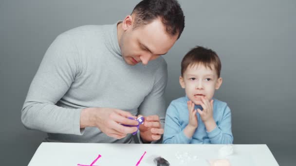 Pai e filho fazendo animais de plasticina em fundo cinza — Vídeo de Stock