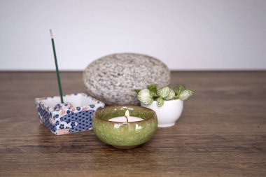 Wellnes arrangement. Burning candle in a ceramic pot, incense sticks, stone and fresh plants on wooden background. Zen style spirituality decoration. Daily meditation routine.