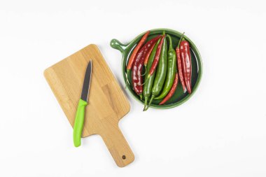 Yeşil ve kırmızı kırmızı biberler yeşil tabakta, kesme tahtası bıçaklı, beyaz arka planda, düz yerde. 