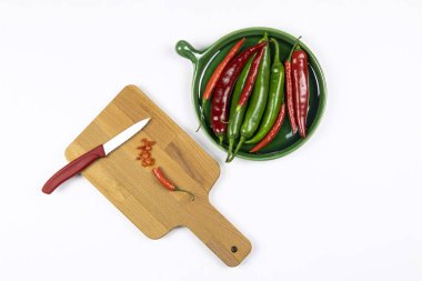 Yeşil ve kırmızı biberler yeşil tabakta, dilimlenmiş biberler tahta tahtada bıçak, beyaz arka plan, doğrama tahtası, düz yatış. 