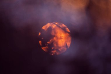 Ağaçların arasından çekilen güzel kırmızı günbatımı. Güzel bir günün sonu. Güneş diski, üzerinde gölgeler olan yakın çekim. Yaz, esrarengiz bokeh arkaplanı.