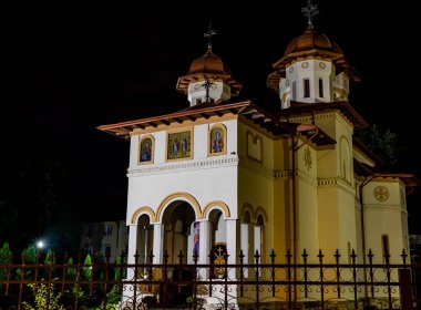 Ön planda boyalı cephe ve çitleri olan kilise geceleri aydınlatılıyor.