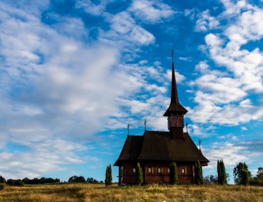 Önünde thuja ağaçları olan eski ahşap kilise Maramures 'da bulutlu mavi bir gökyüzünde.
