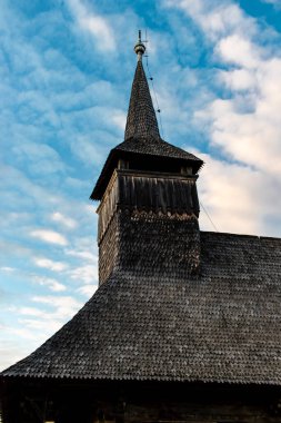 Maramures 'da bulutlu mavi bir günbatımı gökyüzünde eski ahşap bir kilisenin çan kulesinin yukarıdaki görüntüsü.