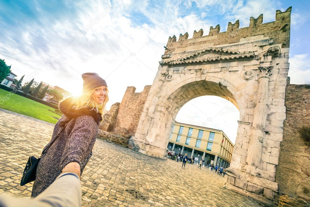 Man following beloved woman on autumn vacation - Fun concept with travelers in Rimini old town at Augustus Arch - Boyfriend and girlfriend around the world - Vivid contrast filter with enhanced sunset
