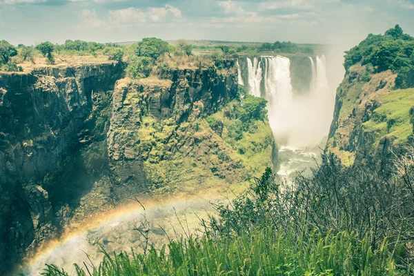 Side view of Victoria Waterfalls with rainbow natural effect - World famous nature wonder of Zimbabwe and Africa continent - Vintage filtered look — Stock Photo, Image