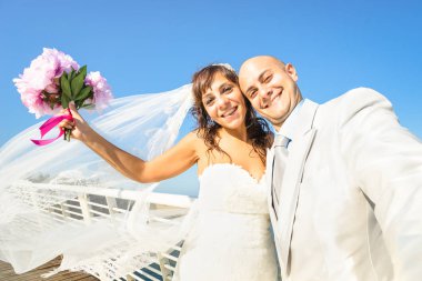 Damat ve gelin sıcak güneşli bir gün sonsuza dek aşk kutlama mavi gökyüzü - birlikte tezahürat Törenden sonra evlilik çift - güzel hayat kavramı karşı selfie alarak buket ile genç yeni evliler