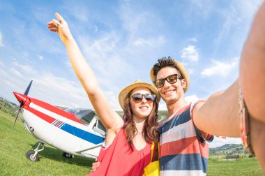 Young couple taking selfie with lightweight airplane - Happy people boarding on excursion air plane - Alternative adventure vacation concept - Warm day colors with tilted horizon fisheye distortion clipart