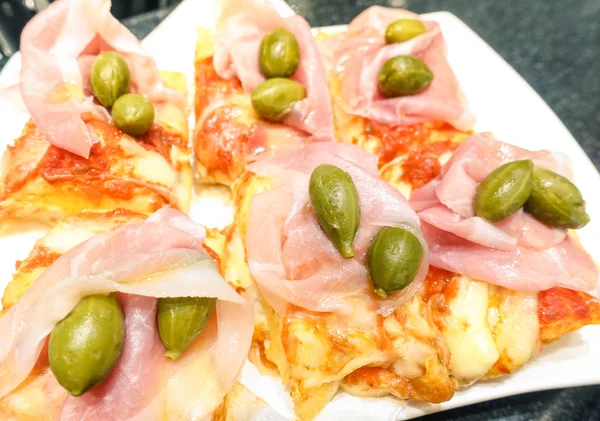 Fatia de refeição de pizza takeaway com presunto de queijo mussarela de tomate e alcaparras - Conceito de lanche alimentar com especialidade italiana caseira - Profundidade de campo rasa com foco no canto inferior direito da imagem — Fotografia de Stock