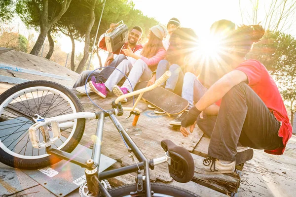 Grupo de amigos de moda divirtiéndose juntos en skate bmx park - Concepto de amistad juvenil con los jóvenes al aire libre - Enfoque en el chico afroamericano con estéreo - Filtro retro vibrante con halo de luz solar   - — Foto de Stock