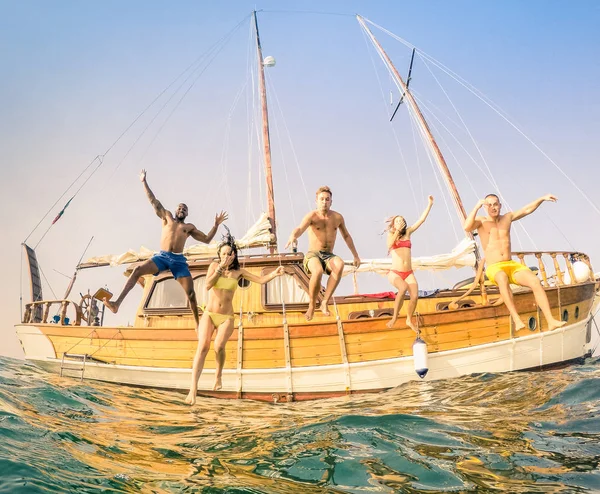 Vista frontal de jóvenes amigos multirraciales saltando desde un velero de madera en un viaje por el mar - Chicos y chicas felices y ricos divirtiéndose en el día de la fiesta de verano - Concepto de vacaciones exclusivas - Filtro vintage cálido —  Fotos de Stock