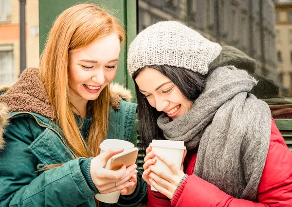 Ευτυχισμένος φίλες διασκεδάζοντας με takeaway καφέ στο Φθινόπωρο σεζόν - έννοια φιλία με χαρούμενη κορίτσια μοιράζονται το χρόνο μαζί με το smartphone και χειμερινά ρούχα - φωτεινά ζωηρά φίλτρο καλύτερος φίλος — Φωτογραφία Αρχείου