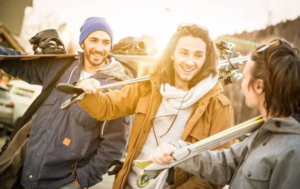 Mejores amigos divirtiéndose juntos caminando con esquí y snowboard en viaje de montaña - Concepto de amistad con los jóvenes pasar el rato amorosos viajes de deportes de invierno - Filtro cálido con luz de fondo halo de sol —  Fotos de Stock