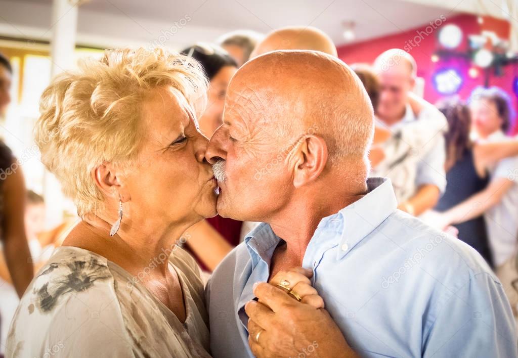 Happy senior retired couple having fun on dancing at restaurant wedding celebration party - Love concept of joyful elderly and retirement lifestyle with man lovely kissing wife - High iso color image