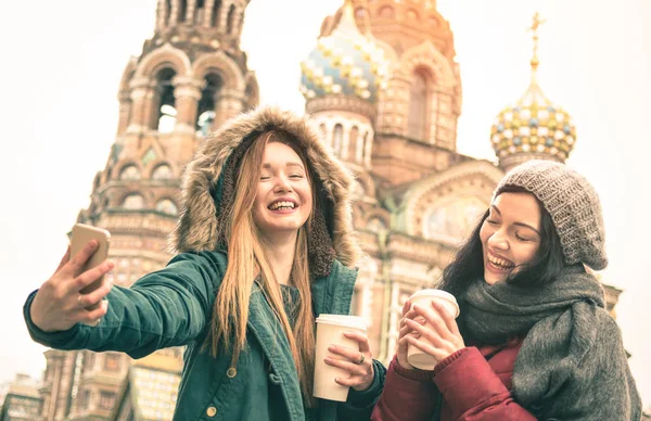 Gelukkig vriendinnen nemen winter selfie op "Verlosser op het Bloed Spilled" kerk in Sint-Petersburg - concept van de vriendschap met meisjes plezier samen drinken koffie outdoor - Focus op linker jonge vrouw — Stockfoto