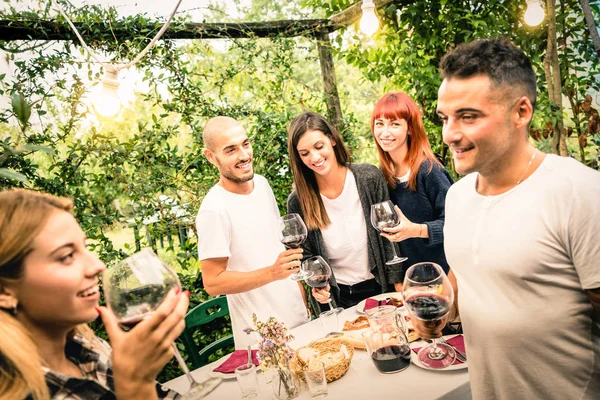 Szczęśliwy znajomych zabawy picie czerwonego wina na podwórku ogród party - koncepcja młodzieży i przyjaźń razem w gospodarstwo winnica winnicy - skupić się na tle młodych ludzi i żarówki lampy oświetlenie — Zdjęcie stockowe