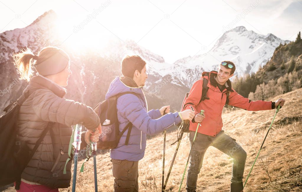 Group of friends trekking on french alps at sunset - Hikers with backpacks and sticks walking on mountain - Wanderlust travel concept with young people at excursion in wild nature - Focus on right guy