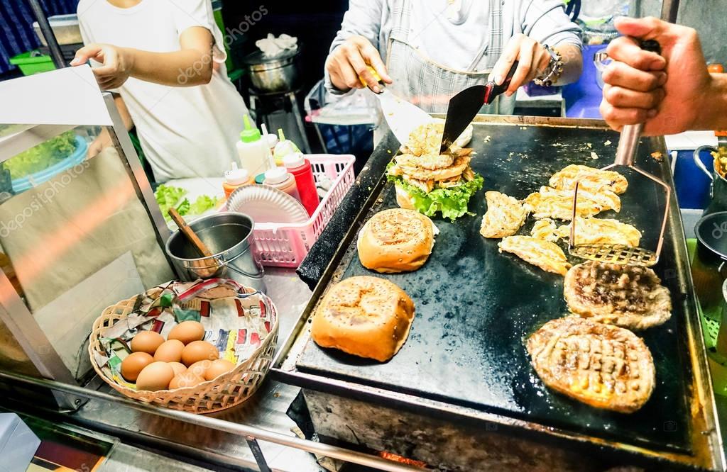 Generic hamburger vendors cooking beef and chicken burgers on grill by night - Street food concept with mobile barbecue station open air in Patong Phuket Thailand - Vivid  incandescent color tones