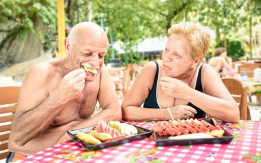 Senior couple having fun eating seasonal fruit in thai restaurant bar outdoors - Mature man and woman on active elderly vacation - Happy retirement concept with people together - Warm shadow filter clipart