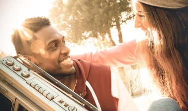 Multiracial couple at beginning of love story listening music on radio stereo recorder - Urban mixed race relationship concept with young people having fun outdoors - Warm desaturated vintage filter clipart