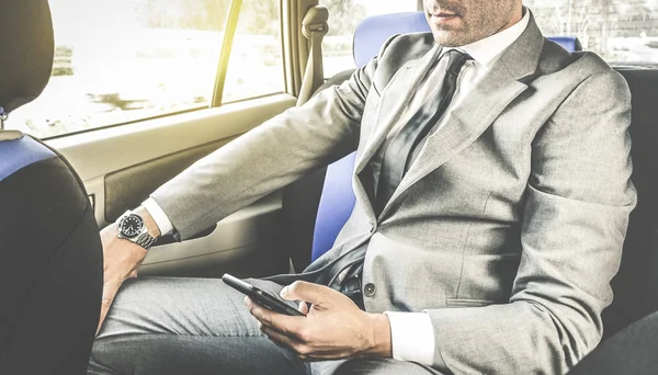 テキスト メッセージの sms のスマート フォン - スマート フォンを使用して現代人のビジネス コンセプト - 柔らかいビンテージ編集ウィンドウから人工的な日光としながらタクシーで座っている若いハンサムな実業家 — ストック写真