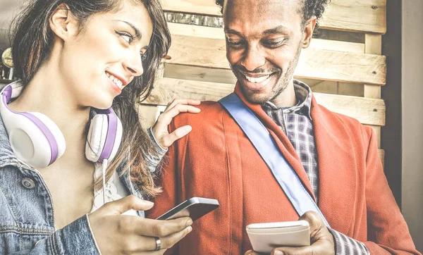 Multiracial couple flirting with smartphone numbers - Modern concept of mobile phone technology with happy people having fun - City urban lifestyle - Retro filter with focus on girl — Stock Photo, Image