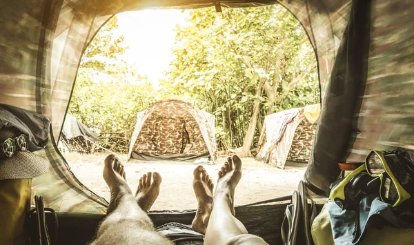 Ponto de vista com o par de pernas dentro da tenda de acampamento - Conceito de desejo de viajar com os jovens desfrutando de experiência de aventura - Bordas borradas com foco suave em pés e filtro de vegetação retro — Fotografia de Stock