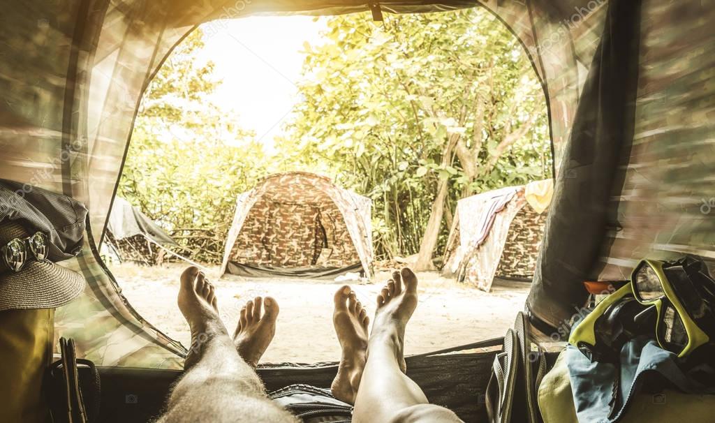 Point of view with couple of legs inside camping tent - Travel wanderlust concept with young people enjoying adventure experience - Blurred edges with soft focus on feet and retro greenery filter