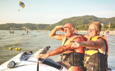 Eğleniyor jet ski üzerinde tur - etkin yaşlı ve seyahat kavramı emekli insanlar binme su scooter jetski ile dünya çapında - sıcak vintage canlı filtre atlamalı beach Adası'nda kıdemli mutlu çift
