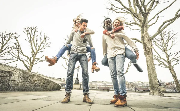 Happy multiracial friends couples having fun with piggiback in winter time waiting spring - Friendship concept with multicultural young people with funny attitude - Retro desaturated contrast filter — Stock Photo, Image