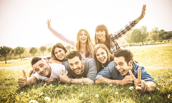 Gruppen av vänner att ha kul tillsammans med självporträtt på gräs äng - vänskap ungdomskoncept med glada ungdomar på picnic camping utomhus - varm vintage filter med bakgrundsbelysning kontrast sunshine — Stockfoto