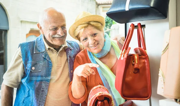 Senior couple shopping at fashion bag store with wife pointing showcase to husband - Active elderly concept with mature man and woman having fun in city - Happy retired people moments on vivid colors — Stock Photo, Image