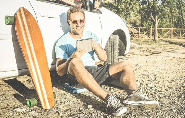 Young hipster fashion guy working remote on computer tablet sitting at car on road trip - New trend and technology concept with digital nomad lifestyle - Traveler man on retro contrasted filtered look — Stock Photo, Image